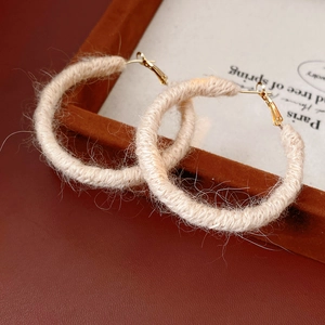 Dettaglio macro di orecchini a cerchio in lana beige su vassoio in legno vintage