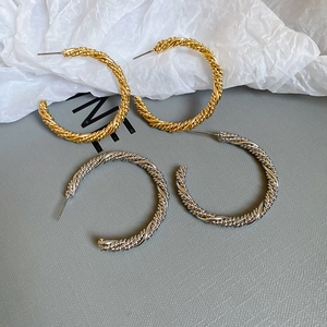 Detailed view of twisted gold and silver C-shape earrings on a textured paper background