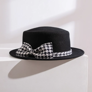 Chapeau canotier noir en laine avec ruban pied-de-poule et nœud sur socle blanc