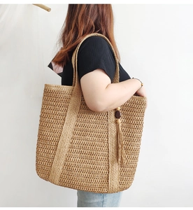 Detailed view of khaki woven tote bag with fringe tassel on shoulder of female model