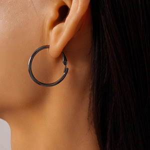 Close-up of minimalist large black metallic hoop earrings worn by a model in detail