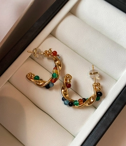 Detail of gold C-shaped earrings with multi-colored beads on a white leather base