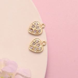 Golden heart-shaped rhinestone pendants for DIY jewelry making on soft pink background