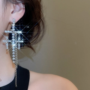 Detailed close-up of silver cross tassel earring with sparkling rhinestones on model