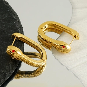 Golden snake hoop earrings with red gem eyes and detailed scale texture on dark rock