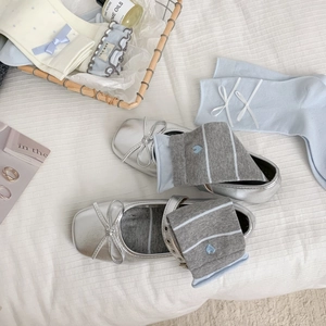 Ballerines argentées à nœud et chaussettes brodées sur un lit blanc moelleux