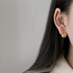 Macro shot of minimalist gold spherical earrings and floral stud on model's ear