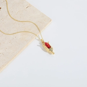 Detailed view of a gold corn cob pendant with red beads on a minimalist stone base