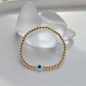 Detail of gold beaded bracelet with classic evil eye charm on a white stone stand