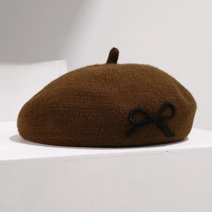 Gros plan sur un béret en maille marron avec un détail de nœud en cuir noir