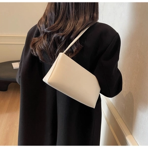 Close-up of a minimalist cream-colored leather underarm bag worn over a black coat