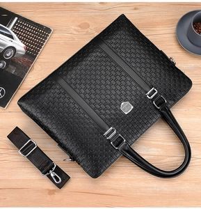 Top view of black leather briefcase with embossed patterns and shoulder strap on wooden desk