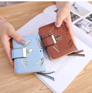 Detail of short leather wallets with leaf cutout design and metallic leaf pendant clasp