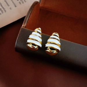 Macro detail of gold-plated conch spiral earrings with white enamel on leather surface