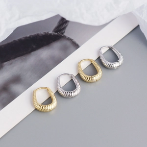 Detailed view of U-shaped gold and silver earrings featuring minimalist twisted textures