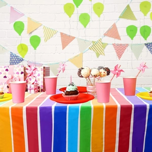 Vibrant party scene showing rainbow striped tablecloth with pink cups and colorful plates