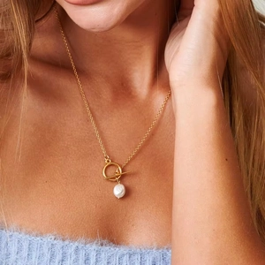 Close-up of gold T-bar toggle necklace with freshwater pearl pendant on model neck