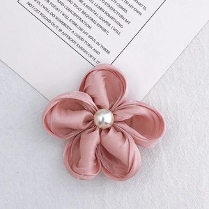 Detail of pink satin flower charm with pearl center on a minimalist white backdrop