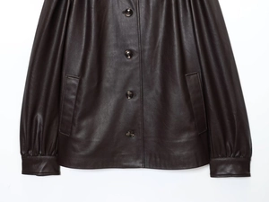 Detailed close-up of dark brown leather jacket featuring round metallic buttons and side pockets