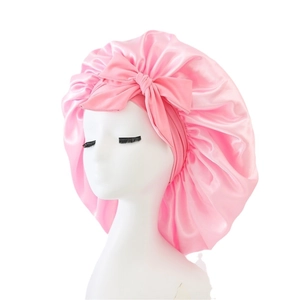 Pink satin sleep cap with large bow for hair protection on white background