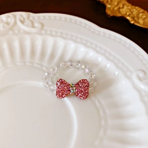 Close-up of beaded crystal ring with a pink rhinestone bow on a white vintage plate