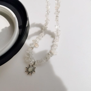 Minimalist crushed stone sunflower necklace with a silver pendant on white surface