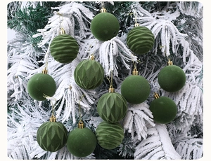 Close-up of green flocked Christmas baubles with various textures on a snowy tree branch