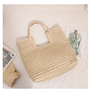 Close-up of beige woven straw tote bag with light brown faux leather handles