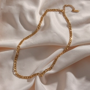 Macro detail of 18K gold plated Figaro chain with K18 engraved tag on silk background