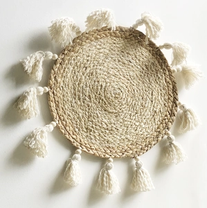 Dettaglio di decorazione murale boho con trama in paglia naturale e nappe eleganti