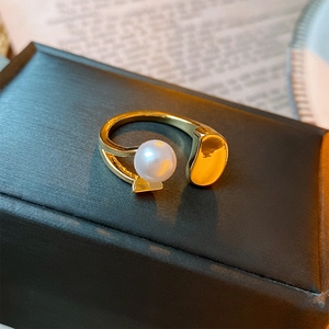 Macro view of gold open ring featuring a white pearl and smooth metallic bean detail