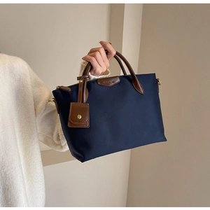 Macro view of blue nylon crossbody bag with leather handles and debossed brand logo