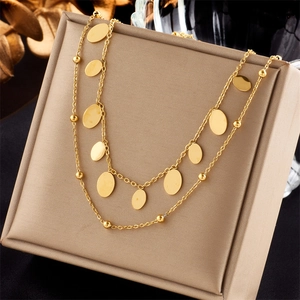 Detail view of double-layer gold necklace with round charms and beads on jewelry box