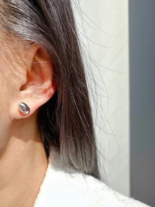 Close-up of minimalist silver bean stud earring worn on ear with polished oval finish