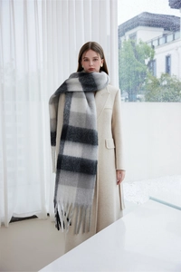Black white and grey checkered scarf with fringe tassels worn by a model in a rainy setting