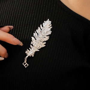 Macro detail of a silver feather brooch with diamonds pinned on black knit fabric