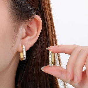 Macro detail of gold-plated rectangular huggie earrings with sparkling baguette zircons