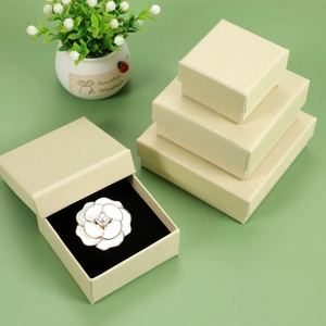 Elegant beige square gift box set with white camellia pearl brooch on a green surface