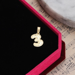 Macro shot of gold number 3 pendant with honeycomb texture in a red velvet jewelry box