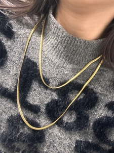 Detail of elegant gold snake bone chain necklaces layered on a leopard pattern sweater