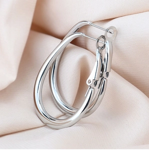 Macro shot of silver-toned oval hoop earrings resting on champagne gold pleated silk fabric