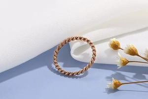 Detail of rose gold twisted rope ring resting on white silk with dried flowers