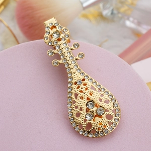 Golden pipa musical instrument hair clip with sparkling rhinestones on pink display base