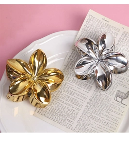 Detailed close-up of metallic flower hair claws in gold and silver finish on a plate