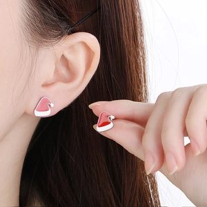 Detail view of red and white enamel Santa hat stud earrings on a model's ear