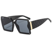 Detail of oversized retro sunglasses with black frames and gold diamond-pattern temples