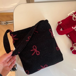 Détail du sac en tricot noir avec nœuds rouges brodés et étiquette de marque latérale