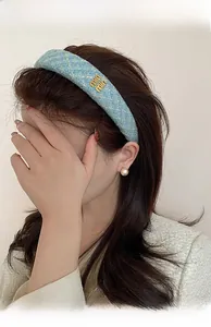 Dettaglio di un cerchietto imbottito in tessuto azzurro con logo dorato indossato dal modello