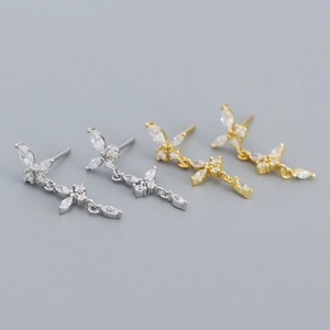 Détail macro de boucles d'oreilles papillon et croix en argent et or avec zircons brillants