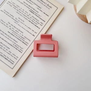 Pink rectangular matte hair claw clip on an open book showing a minimalist hollow design